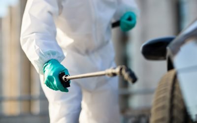 Close-up of man in protective suit disinfecting car tire during coronavirus epidemic.