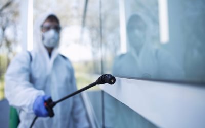 Person in white chemical protection suit doing disinfection of public areas to stop spreading highly contagious corona virus.